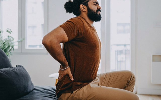 Man experiencing lower back pain while standing up, indicating possible spine or muscle strain issue